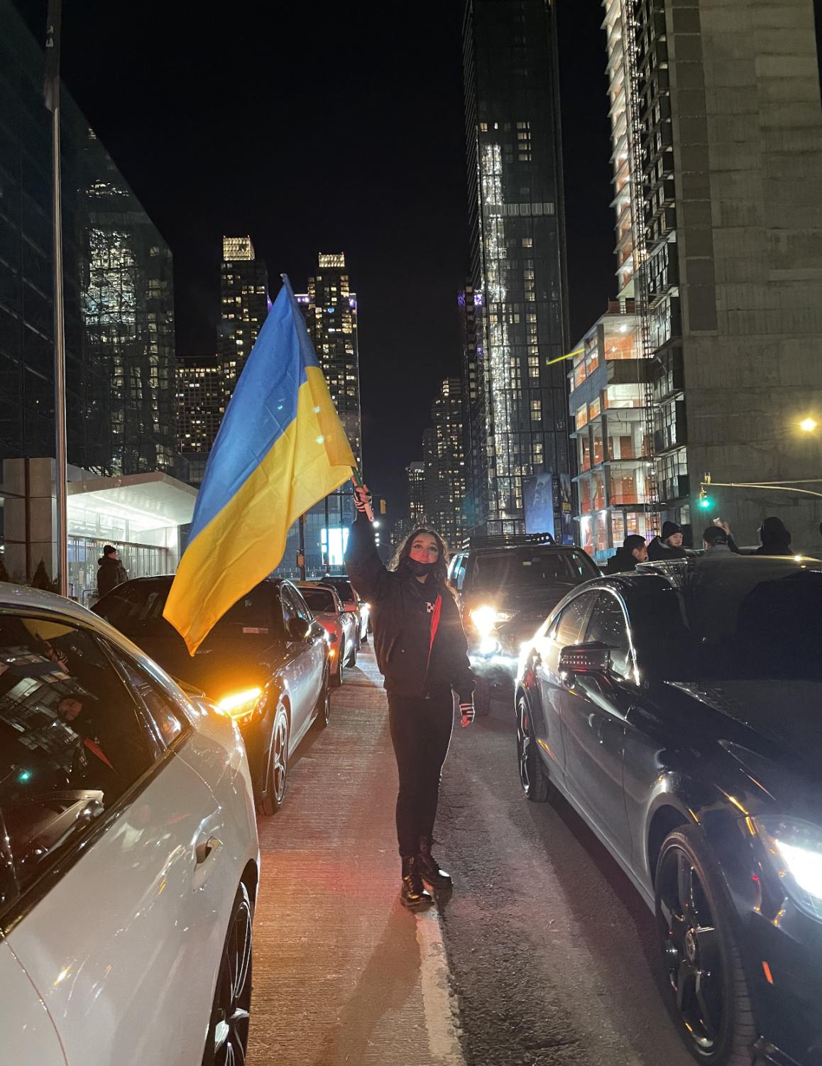 girl stands in the street of times square with cars around holding a ukrainian flag